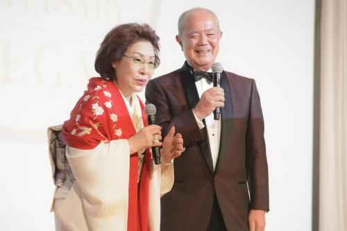恒例の掛け合いトークであいさつする濱野隆一郎会長夫妻