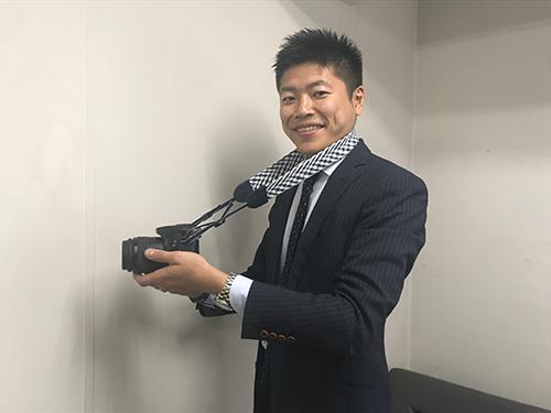 萩島貴社長。「ブルー」のストラップをかけている
