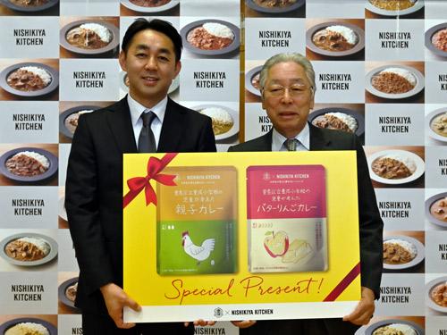 児童に商品を贈る菊池洋代表（写真右）と豊成小学校の山本知範校長